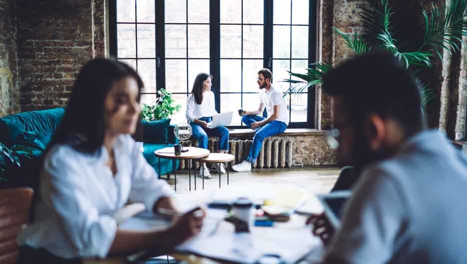 Side view of focused multiethnic colleagues in casual wear sitting in modern office and discussing details of business project together